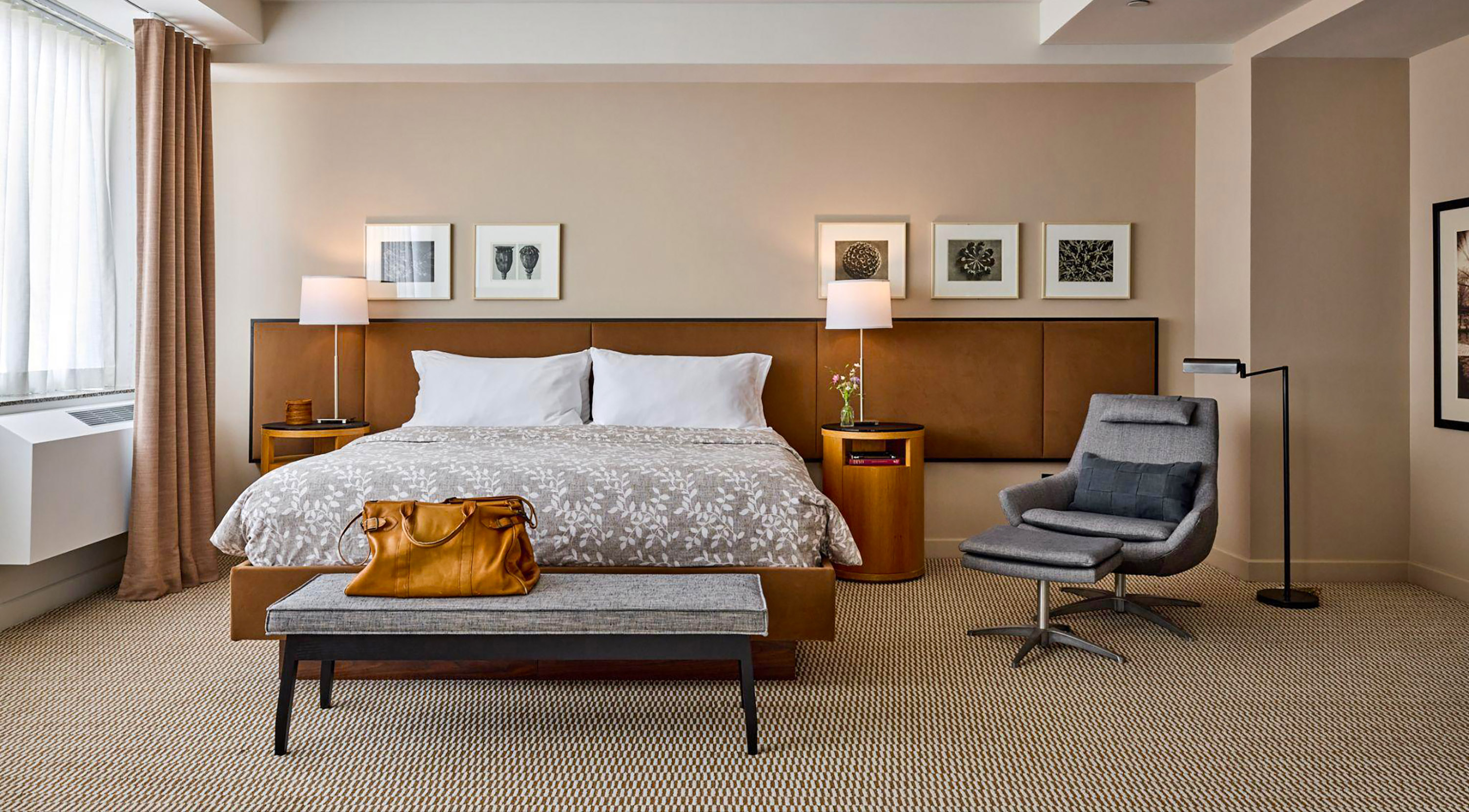 A wide view of a hotel room with a bed, chair, bench, and nightstands.
