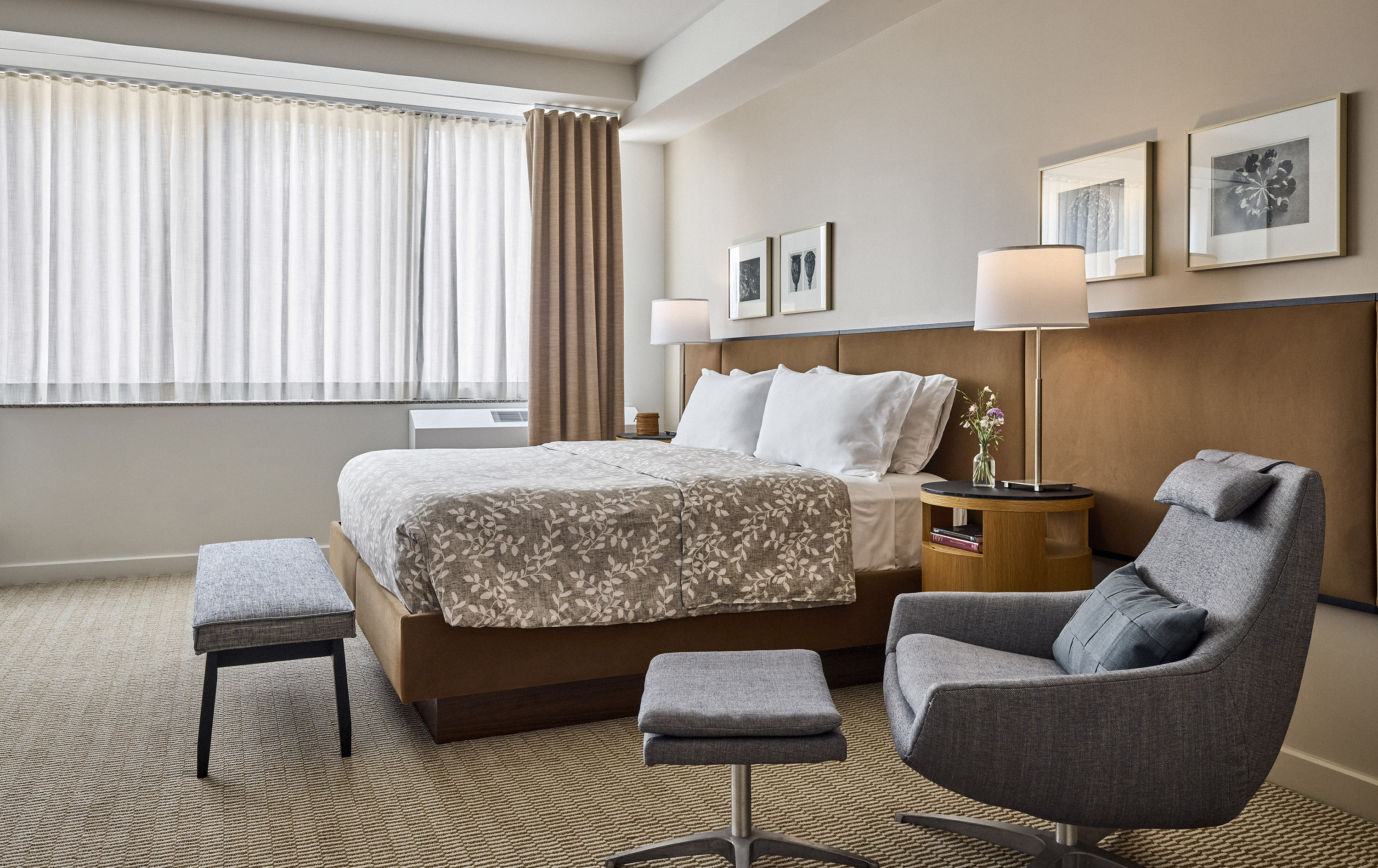 A hotel room with a bed, chair, window, and nightstand.