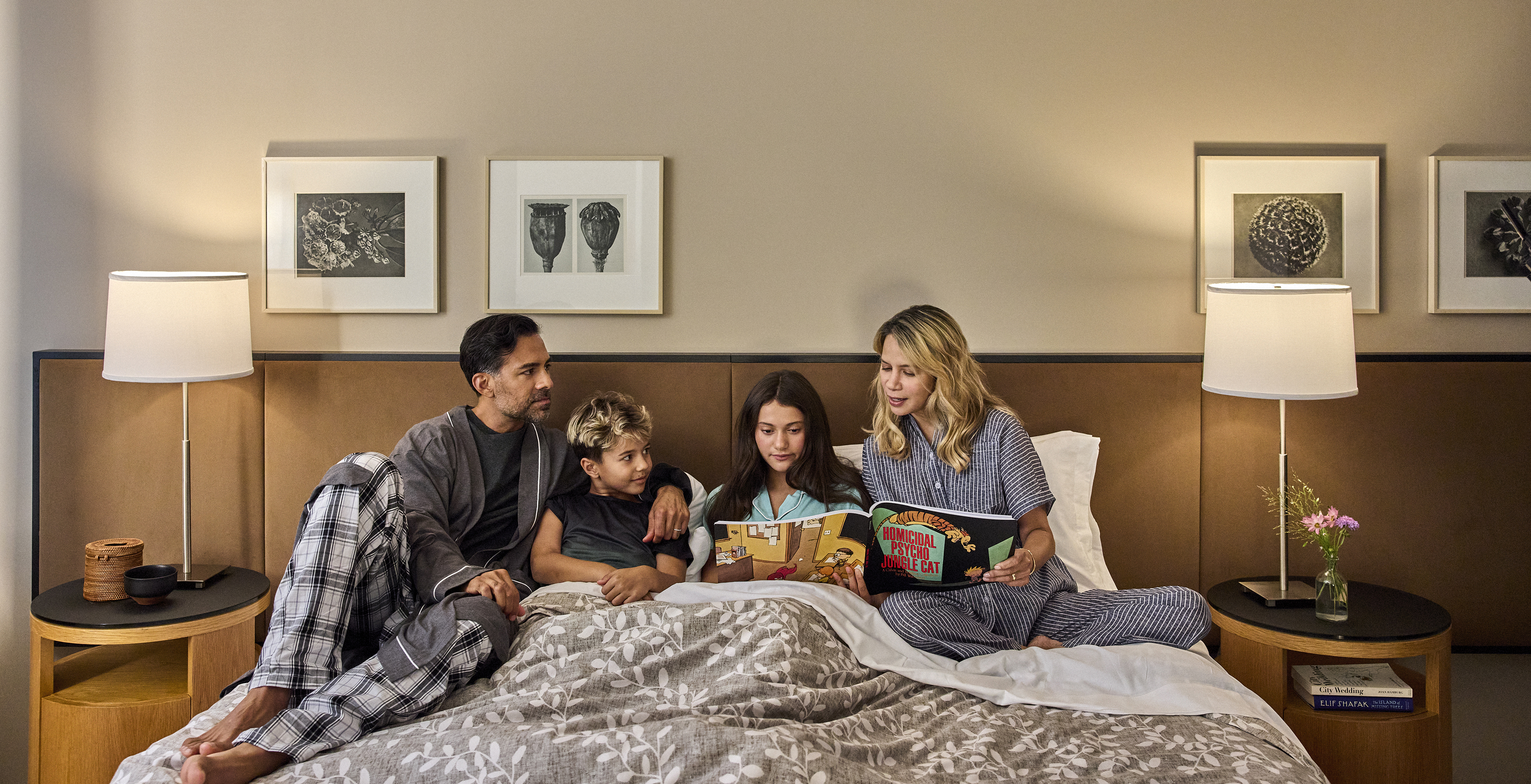 A family of four is sitting on a bed in a hotel room.